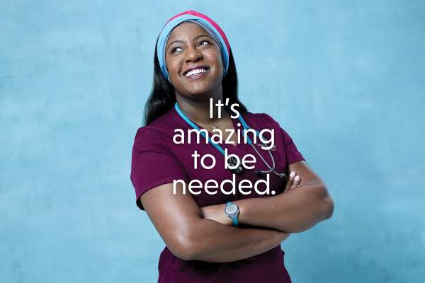 Text: It's amazing to be needed. A black woman in nurse's scrubs and a colorful head scarf.