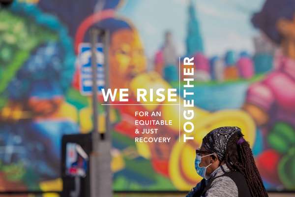 Image text: We Rise Together. A Black woman in a face mask contemplates a mural in Chicago.
