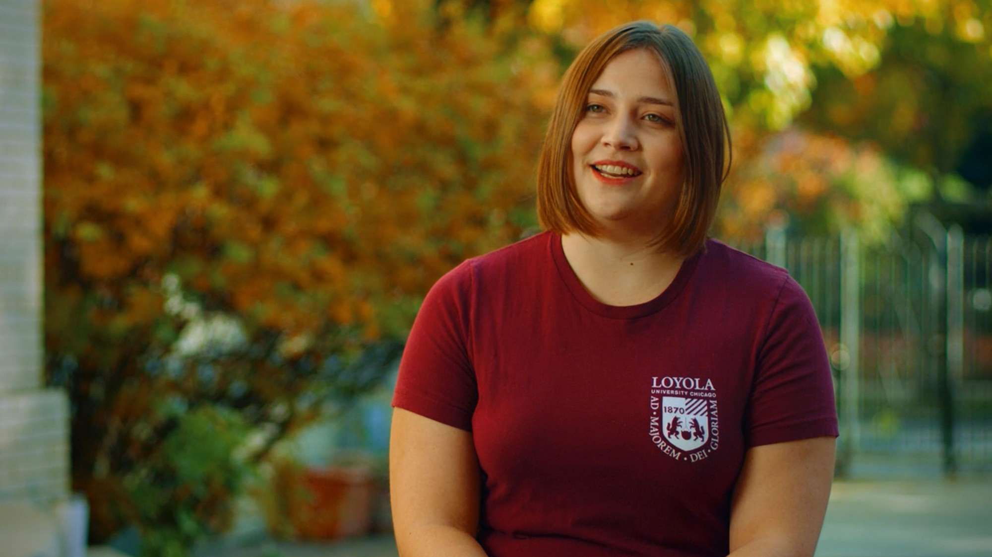 Still scene from a video; a college-age woman in a Loyola shirt addresses the camera.