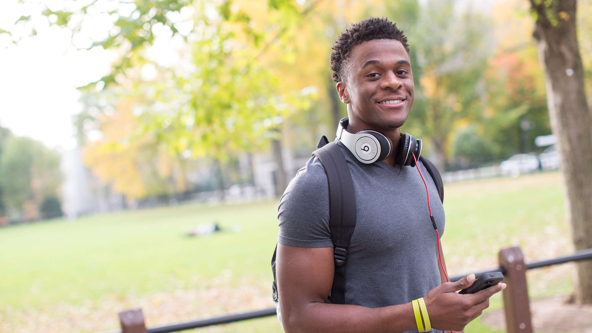 male student in park with headphones around his neck
